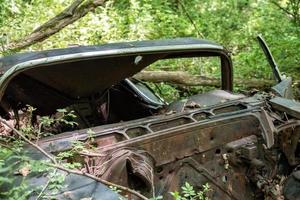 Altes verrostetes Auto, das im Wald mit Einschusslöchern aufgegeben wurde foto