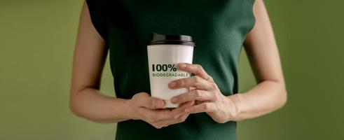 biologisch abbaubares und kompostierbares Verpackungskonzept. Nahaufnahme einer Frau, die eine heiße Tasse Kaffee gegen eine grüne Wand hält. null Abfallmaterialien. Umweltpflege, Wiederverwendung, erneuerbar für einen nachhaltigen Lebensstil foto