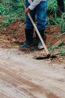 Nicht identifizierbarer Landarbeiter, der Unkraut mit einer Hacke in einem Bauernhof schneidet foto