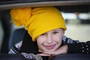 positiver kleiner junge in einer gelben strickmütze schaut auf die kamera und lächelt. Porträt eines zehnjährigen Jungen. Kind im Autofenster. foto