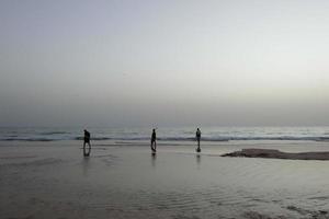 Einsamer Strand mit Menschen, die auf dem Sand am Rand der Meereswellen spazieren gehen foto