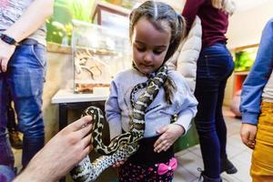 Zoo-Freiwilliger zeigt einem Kind eine Schlange und lässt es die Schlange berühren foto