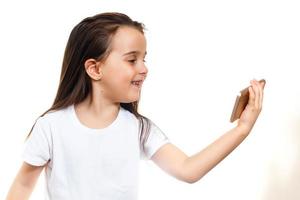 Kleines Mädchen schaut den Cartoon auf dem Handy im Hintergrundkonzept der weißen Wand foto