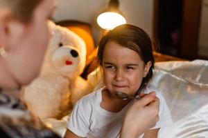 krankes kleines Mädchen im Bett, das Medizin mit Löffel nimmt foto