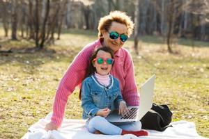 hübsches kleines Mädchen, das im Park mit dem Laptop ihrer Großmutter spielt foto