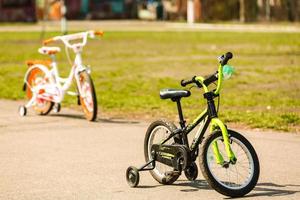 Ein niedriges zweirädriges weiß-lila Kinderfahrrad mit zusätzlichen Seitenrädern steht mitten im Park und lebt seinen kleinen Besitzer. foto