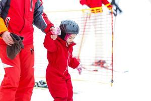 kleines Mädchen in Rot, das mit Hilfe eines Erwachsenen Skifahren lernt foto