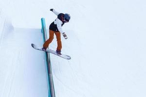 Ein mutiger Mann führt eine Schienenrutsche auf dem Snowboard durch foto