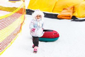 kleines Mädchen mit Snowtube bereit zum Rodeln einen Hügel hinunter foto