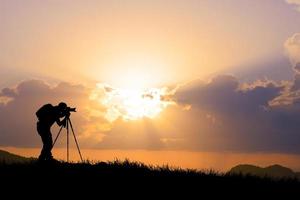 Die Silhouette eines professionellen Fotografen konzentriert sich auf das Fotografieren auf einer wunderschönen Wiese. foto