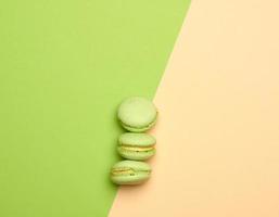 Gebackene grüne Macarons-Kekse liegen in einer Reihe auf einem grün-beigen Hintergrund foto