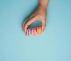 weibliche hand hält drei runde gebackene macarons-kekse auf blauem hintergrund foto