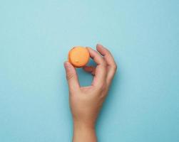 weibliche hand halten rund gebackene orange macaron kekse auf blauem hintergrund foto