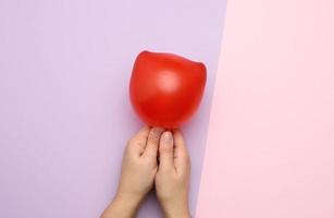 weibliche hand, die einen aufgeblasenen roten luftballon auf einem rosa hintergrund hält foto