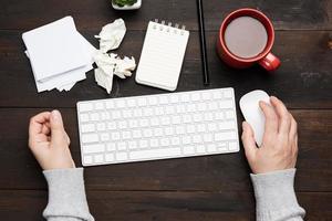 Weiße kabellose Tastatur und Maus auf einem braunen Holztisch, neben einer weißen Tasse mit Kaffee foto