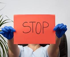 Die Sanitäterin sitzt in einem braunen Lederstuhl im Büro und hält ein rotes Blatt Papier mit der Aufschrift Stopp foto