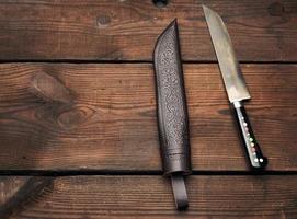 uigurisches usbekisches traditionelles universelles scharfes Messer mit schwarzem Griff auf braunem Holzhintergrund foto