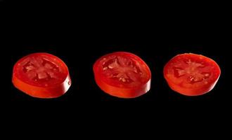 drei Scheiben rote reife Tomaten auf schwarzem Hintergrund isoliert foto