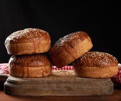 Gebackene runde knusprige Sesambrötchen für Burger auf braunem Holzbrett foto