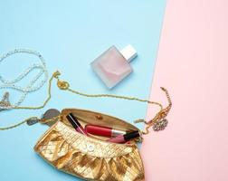 goldene handtasche, lipgloss und perlen auf blauem hintergrund foto