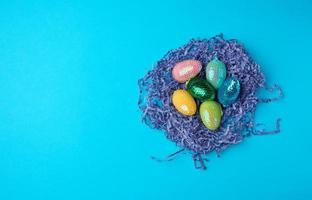 dekorative ostereier aus pailletten liegen in einem nest aus papierstreifen auf blauem hintergrund foto