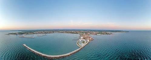 Drohnenpanorama der kroatischen Küstenstadt Umag bei Sonnenuntergang über der Hafeneinfahrt mit Wellenbrecher foto