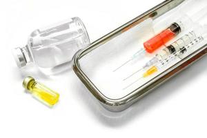 Impfstoff in Fläschchen und Kunststoffspritzen mit medizinischen Nadeln in einem medizinischen Edelstahlbehälter zur fertigen Injektion an den Patienten auf weißem Hintergrund.