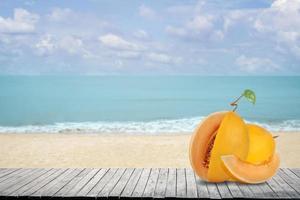 Orangenmelone oder Cantaloupe-Melone auf dem Schreibtisch aus Holz und Hintergrund des Strandes mit Meer und blauem Himmel foto