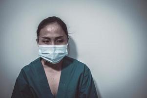 müde depressive asiatische krankenschwester trägt gesichtsmaske blaue uniform sitzt auf dem krankenhausboden, junge ärztin gestresst von harter arbeit foto