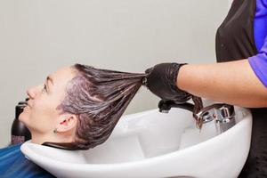 der friseur in schwarzen handschuhen wäscht die haare der brünetten frau im schönheitssalon. foto