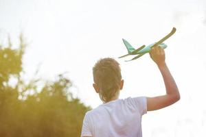 glücklicher kleiner Junge, der bei Sonnenuntergang mit Spielzeugflugzeug im Freien spielt foto