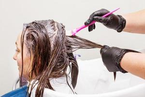 der friseur in schwarzen handschuhen malt im schönheitssalon die haare einer brünetten frau. foto