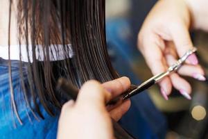 Haarschnitt in einem Schönheitssalon. die hände des friseurs schneiden brünette haare in der nähe foto