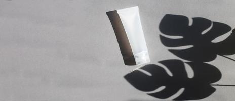 Kunststoffrohr für Creme oder Lotion auf grauem Hintergrund mit Schatten von Montera-Blättern. Beauty-Konzept foto