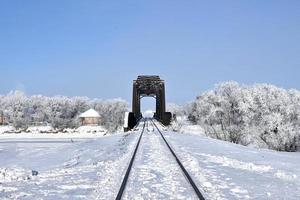 Eisenbahnschienen führen durch den Schnee zu einer Brücke foto