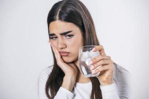 junge Frau mit empfindlichen Zähnen und einer Hand, die ein Glas kaltes Wasser mit Eis hält. Gesundheitskonzept. frau trinkt kaltes getränk, glas voller eiswürfel und fühlt zahnschmerzen, schmerzen foto