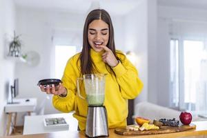 gesunde frau macht gerne grünes gemüse entgiftungsreinigung und grünen frucht-smoothie mit mixer in der küche zu hause. gesunder Lebensstil. schönes Mädchen, das Smoothie schmeckt foto