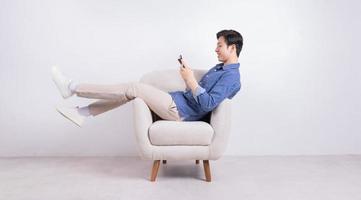 junger asiatischer Mann sitzt auf Sessel auf weißem Hintergrund foto