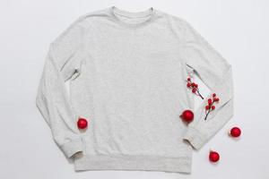 Schließen Sie herauf weißes leeres Schablonensweatshirt mit Kopienraum und Weihnachtsfeiertagskonzept. draufsicht-modell-hoodie und rote feiertagsdekorationen auf weißem hintergrund. frohes neues jahr zubehör. Weihnachts-Outfit foto