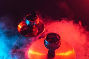 Shisha-Schüssel, Shisha und Kohlen in Nahaufnahme auf einem rauchigen schwarzen Hintergrund mit farbiger Beleuchtung foto
