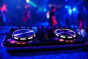 DJ-Konsole zum Mischen von Musik mit verschwommenen Leuten, die auf einer Nachtclubparty tanzen foto