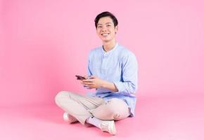 junger asiatischer mann sitzt und benutzt smartphone im hintergrund foto