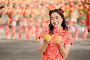 frohes chinesisches neujahr. eine junge dame, die traditionelles cheongsam qipao kleid trägt, das altes goldgeld und orange frisch im chinesischen buddhistischen tempel hält. Feiern Sie das chinesische Neujahrsfest. foto