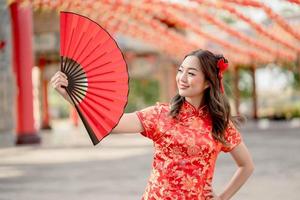 schöne asiatische frau, die traditionelles cheongsam qipao kostüm trägt, das fan im chinesischen buddhistischen tempel hält. Konzept des chinesischen Neujahrsfestes foto