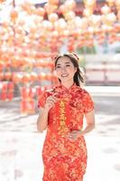 vertikales Bild. frohes chinesisches neujahr. eine junge dame, die traditionelles cheongsam qipao-kleid trägt, das glückskarte im chinesischen buddhistischen tempel hält. chinesischer text bedeutet gesegnet von einem glücksstern foto