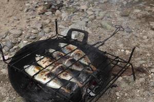 der Prozess der Herstellung von gegrilltem Fisch, der über Kokosnussschalenkohlen verbrannt wird foto