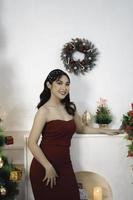 porträt eines hübschen jungen mädchens, das ein rotes kleid trägt, in die kamera lächelt und drinnen in einem dekorierten weihnachtswohnzimmer steht foto