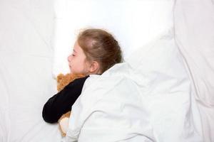 Mädchen, das im Bett schläft und einen Bären umarmt foto