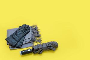 handschuhe, graues tippet und grauer regenschirm auf gelbem hintergrund mit kopienraum foto