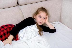 Mädchen mit langen Haaren im Schlafanzug liegt im Bett und sieht sich etwas begeistert an foto